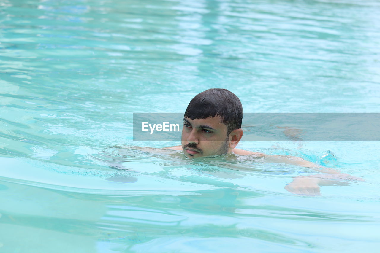 Headshot of a young man swimming in blue water