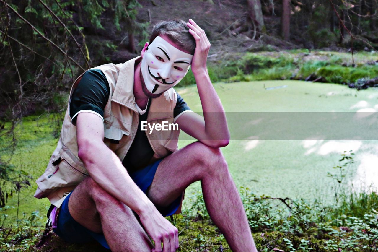 Portrait of man wearing mask sitting by pond