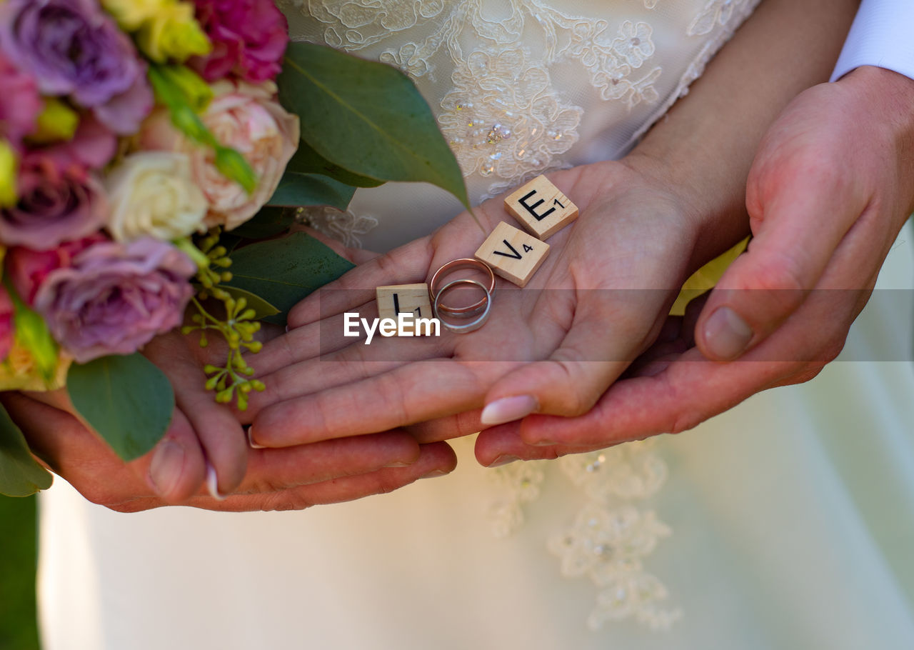 Midsection of couple holding love text with wedding rings