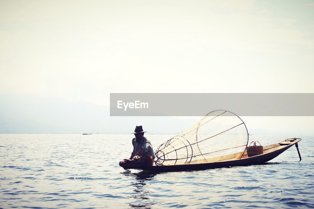 Fisherman rowing boat in sea against sky