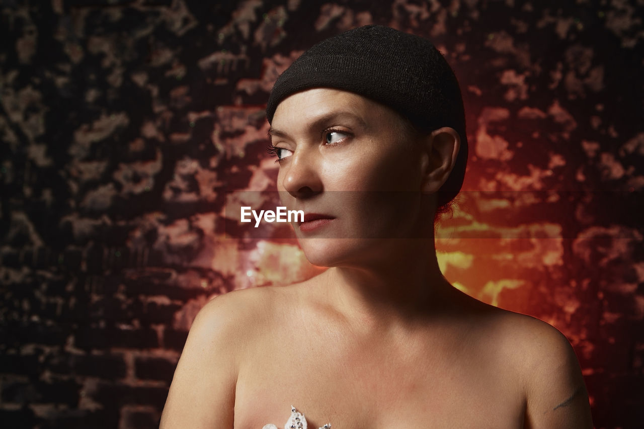 Topless woman looking away against brick wall