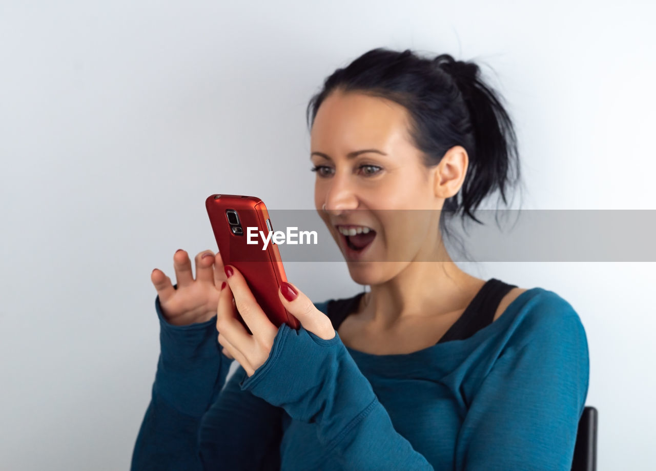 Surprised woman using phone against white background