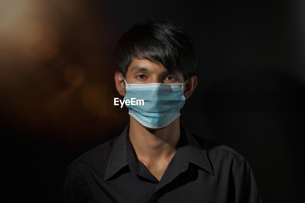 Close-up portrait of man wearing mask against black background