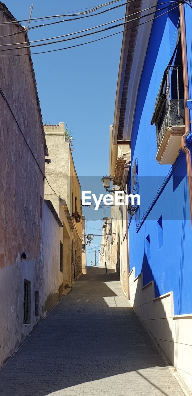 Narrow alley amidst buildings against blue sky, blue casa ,stucco buildings