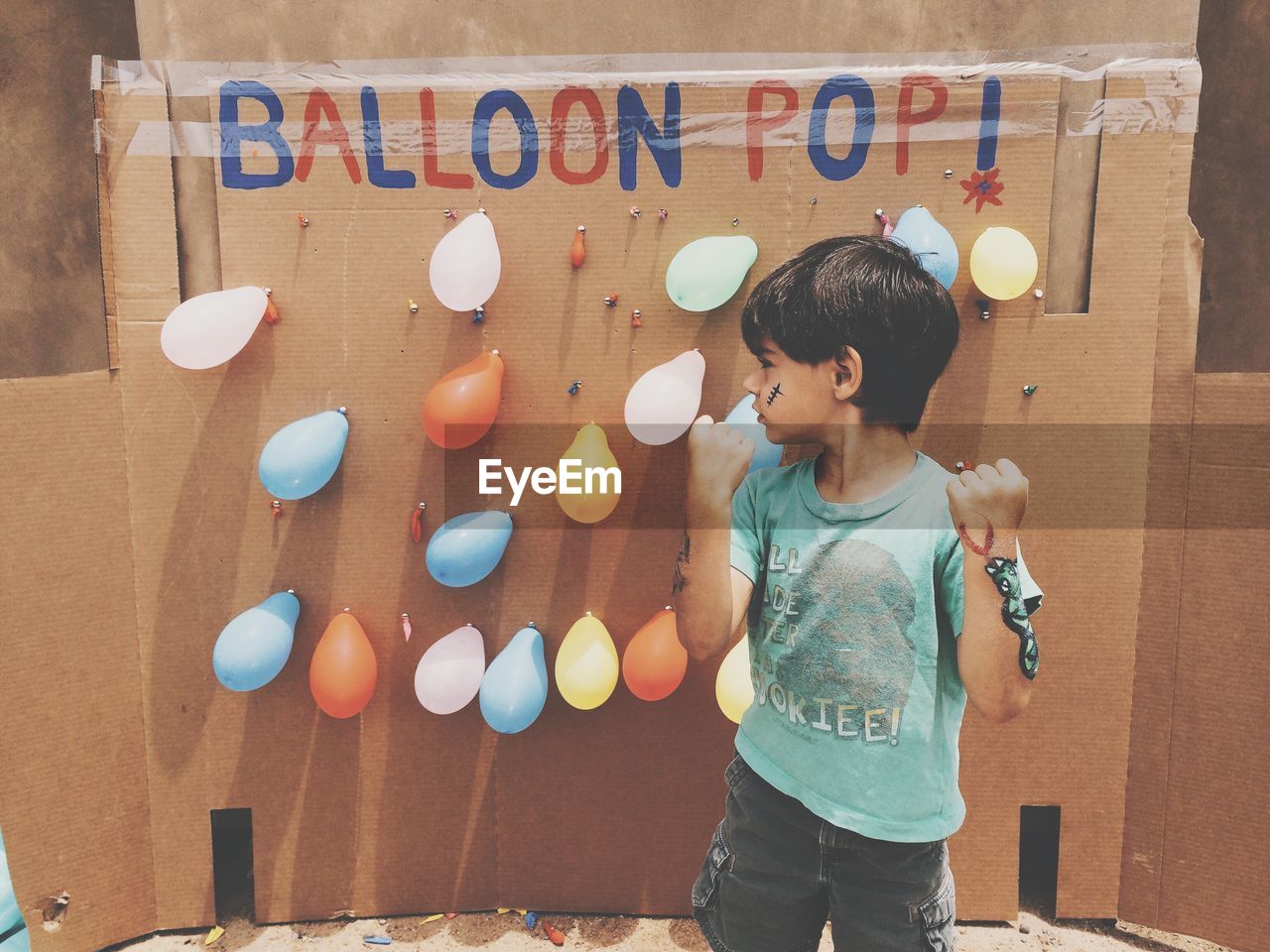 Boy standing against balloons attached on cardboard outdoors