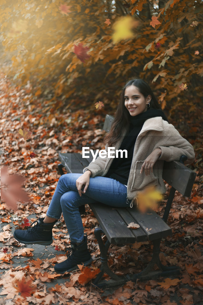 PORTRAIT OF YOUNG WOMAN SITTING ON AUTUMN LEAVES