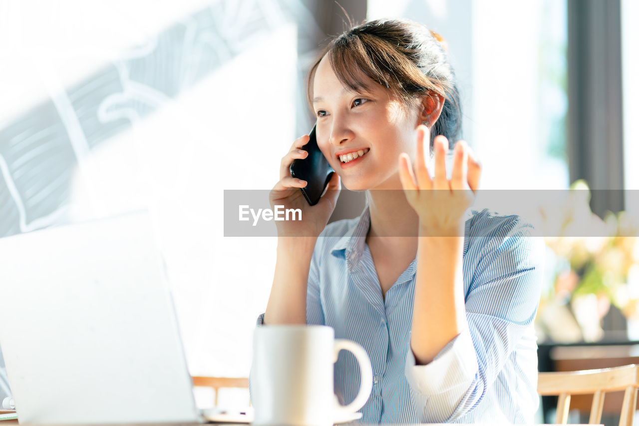 businesswoman talking on phone while sitting on table in office