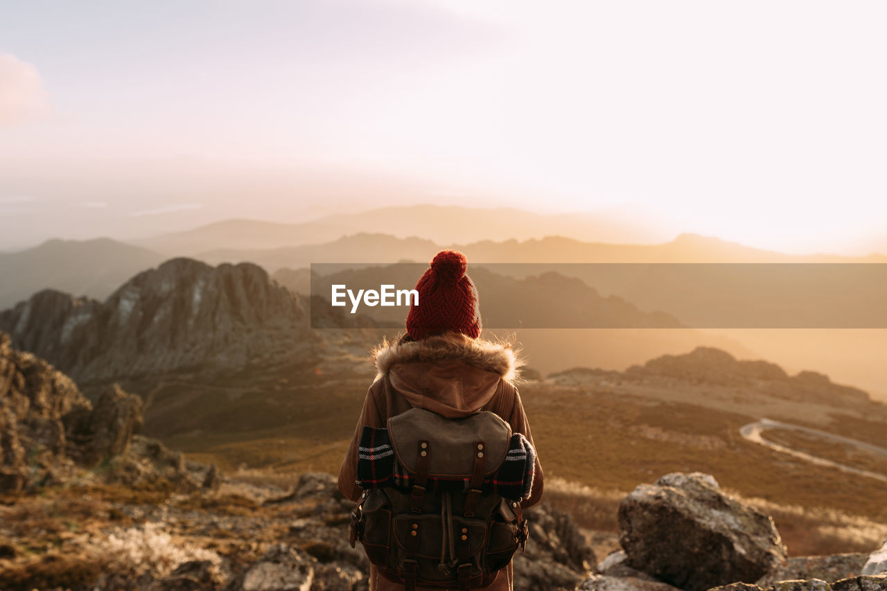 Back view of unrecognizable hiker standing on stone and observing amazing scenery of highlands valley on sunny day