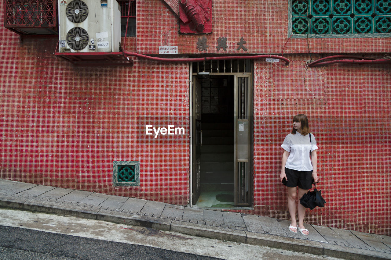 Full length of young woman standing against building