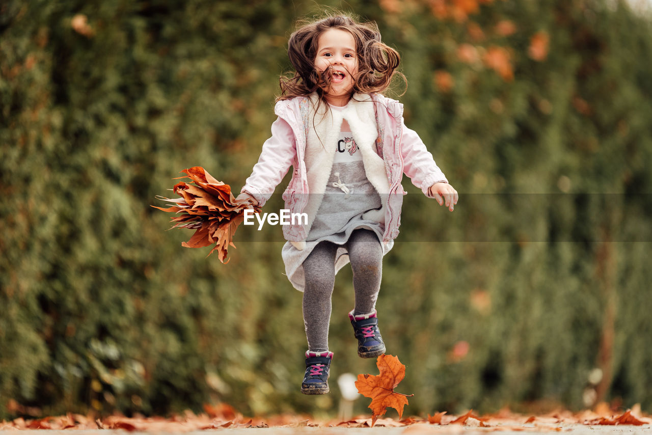 Full length of girl holding leaves jumping at park