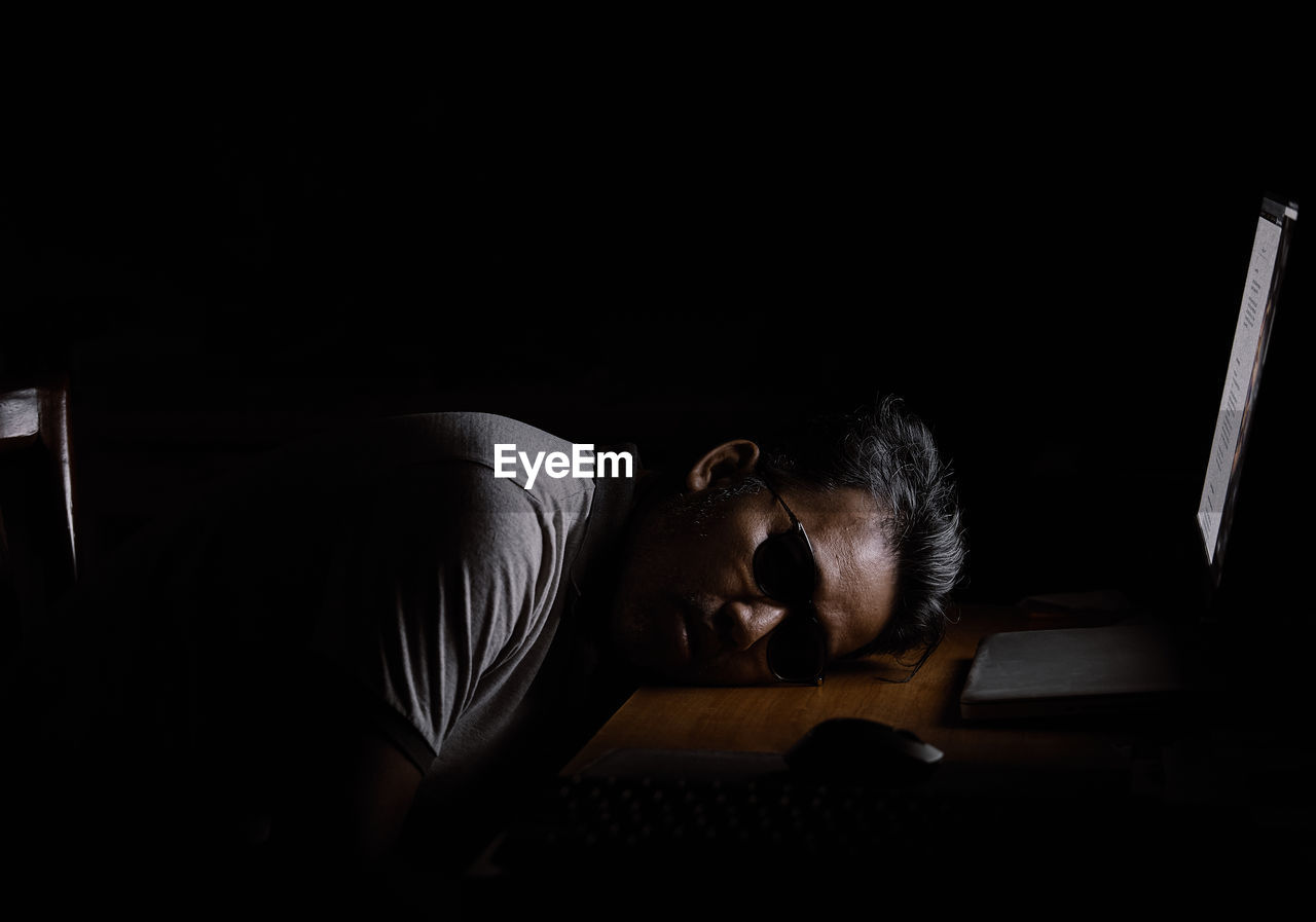 Man sleeping on desk by laptop in darkroom