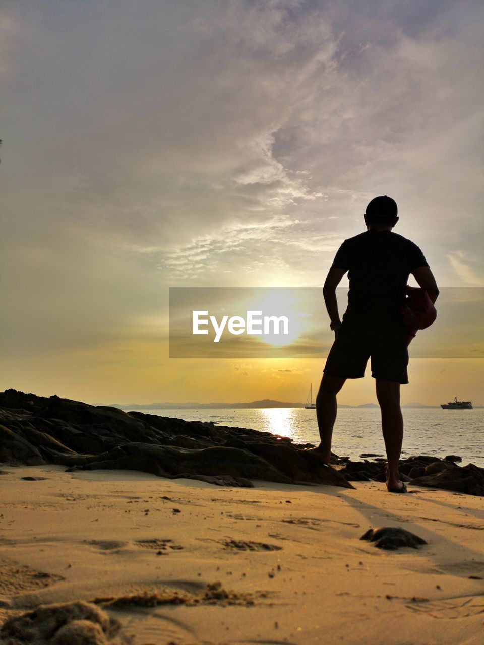 REAR VIEW OF SILHOUETTE MAN STANDING AT BEACH DURING SUNSET