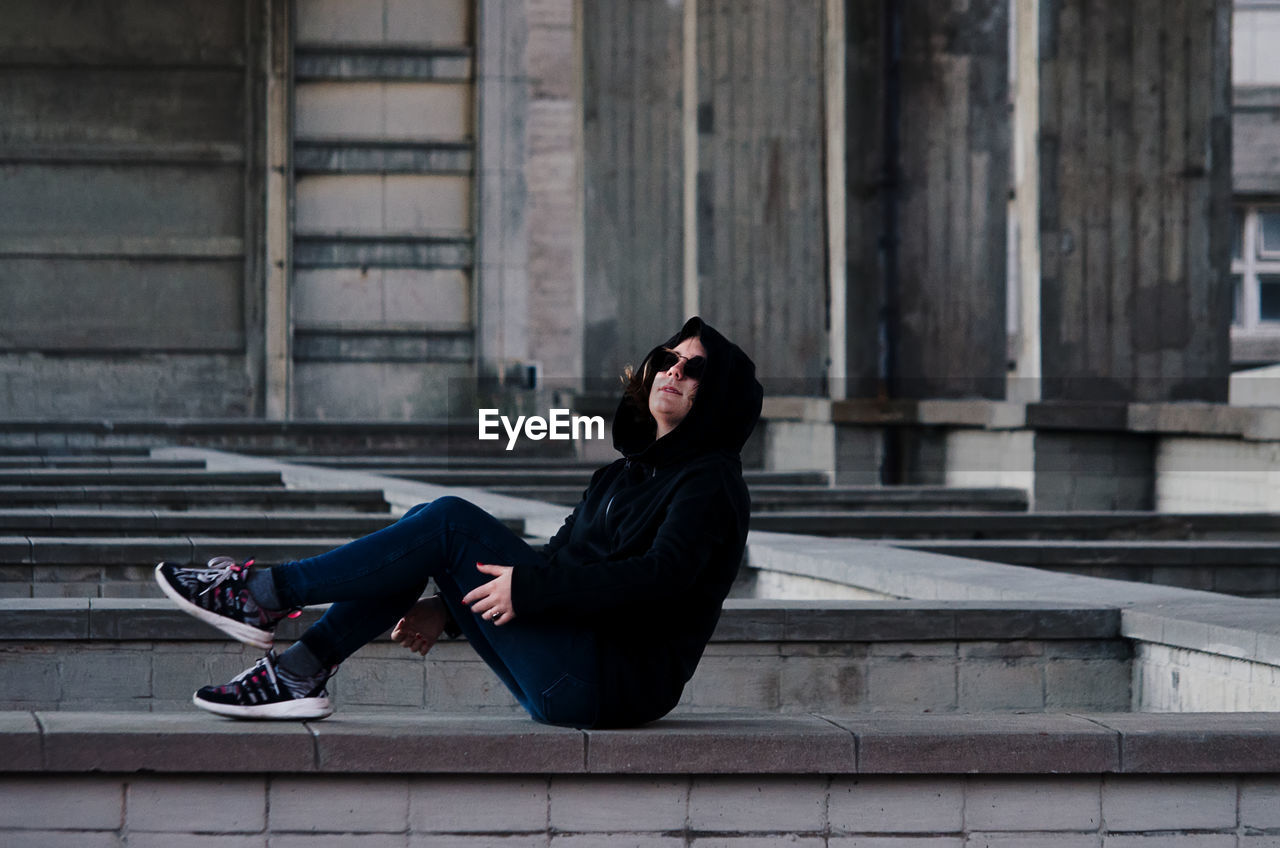 Side view of woman wearing sunglasses while sitting below bridge