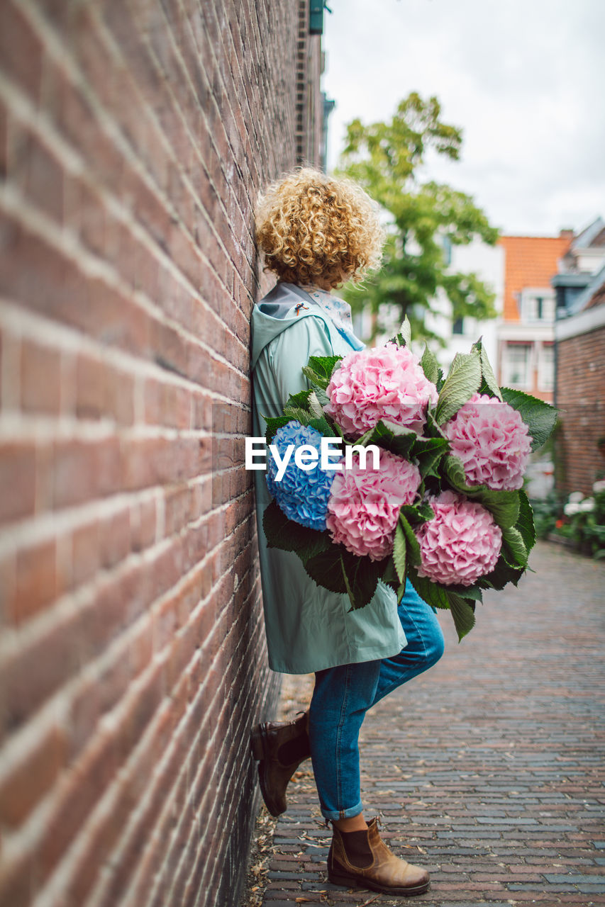 rear view of woman holding bouquet while standing against wall