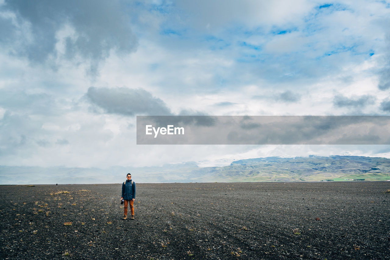 Man with camera standing on field against cloudy sky