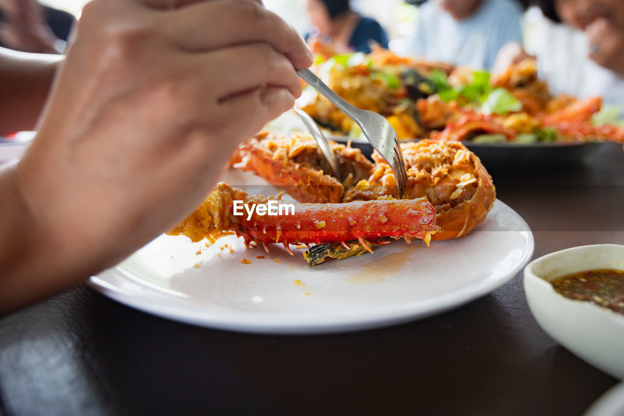 Woman hand holding fork dipping in piece of fried lobster shrimp with garlic on the plate.