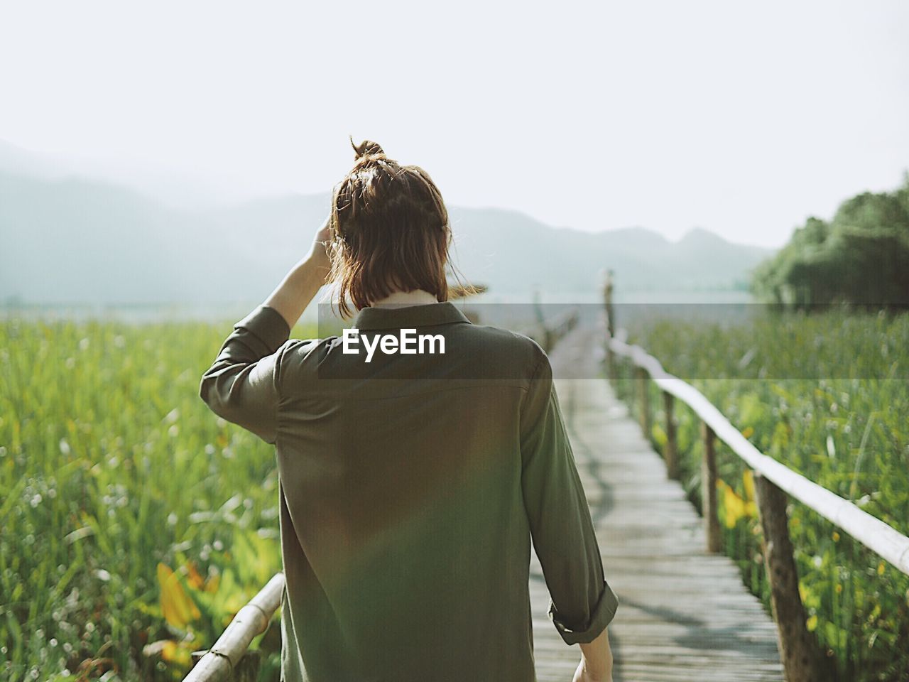 Rear view of woman standing on boardwalk amidst agricultural field