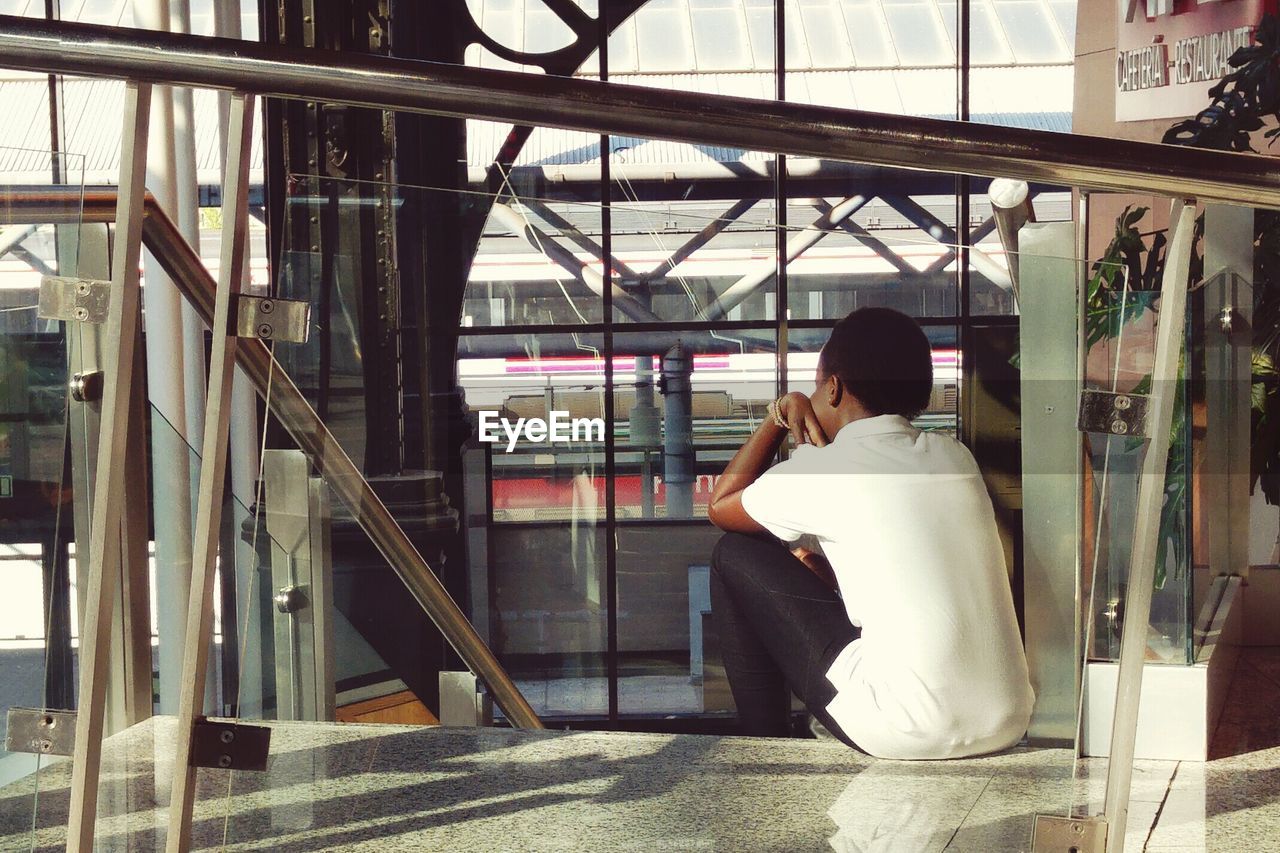 Rear view of woman sitting on steps in railroad station