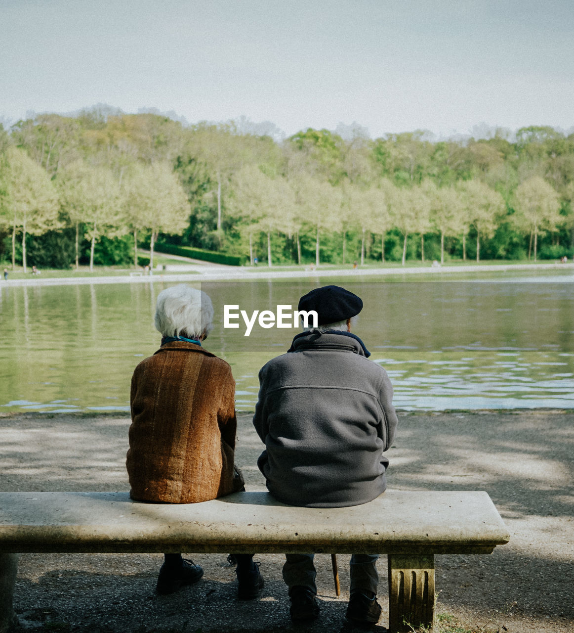 Rear view of couple sitting at lakeshore against sky