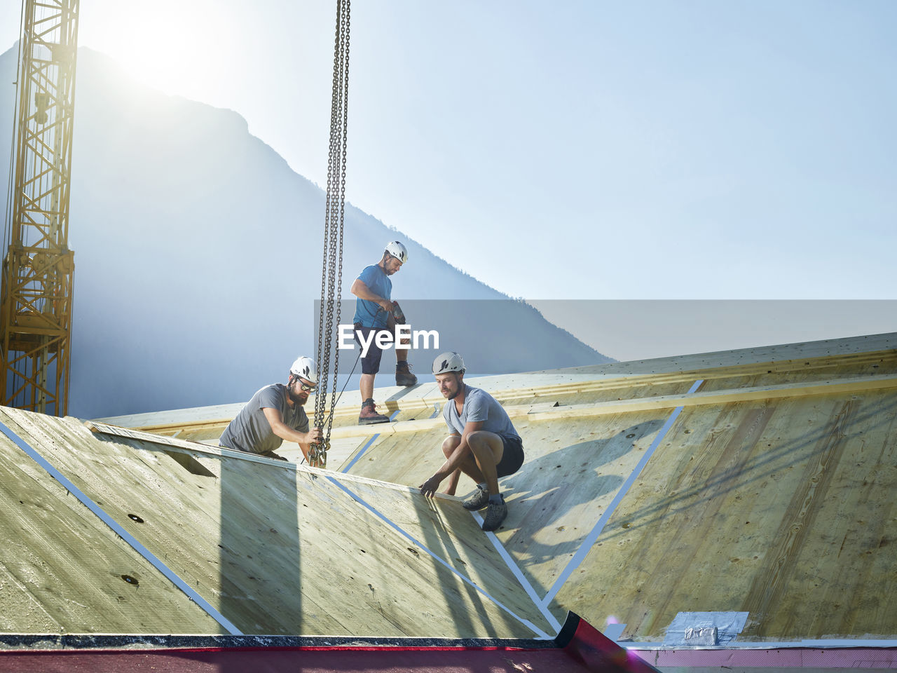 Carpenters working on roof with crane at construction site