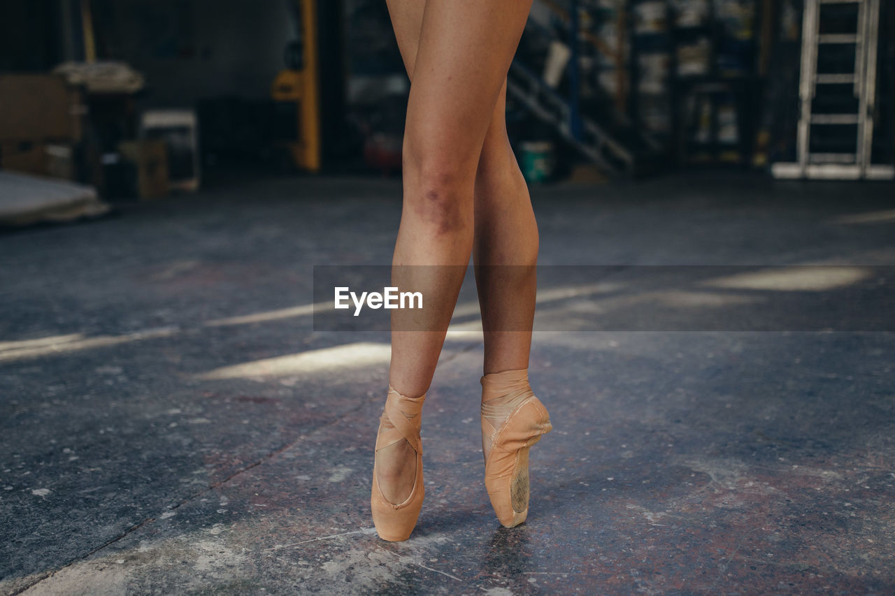 Crop unrecognizable female ballet dancer in pointes with bruise on leg standing on tiptoe while performing classic exercise during training in studio