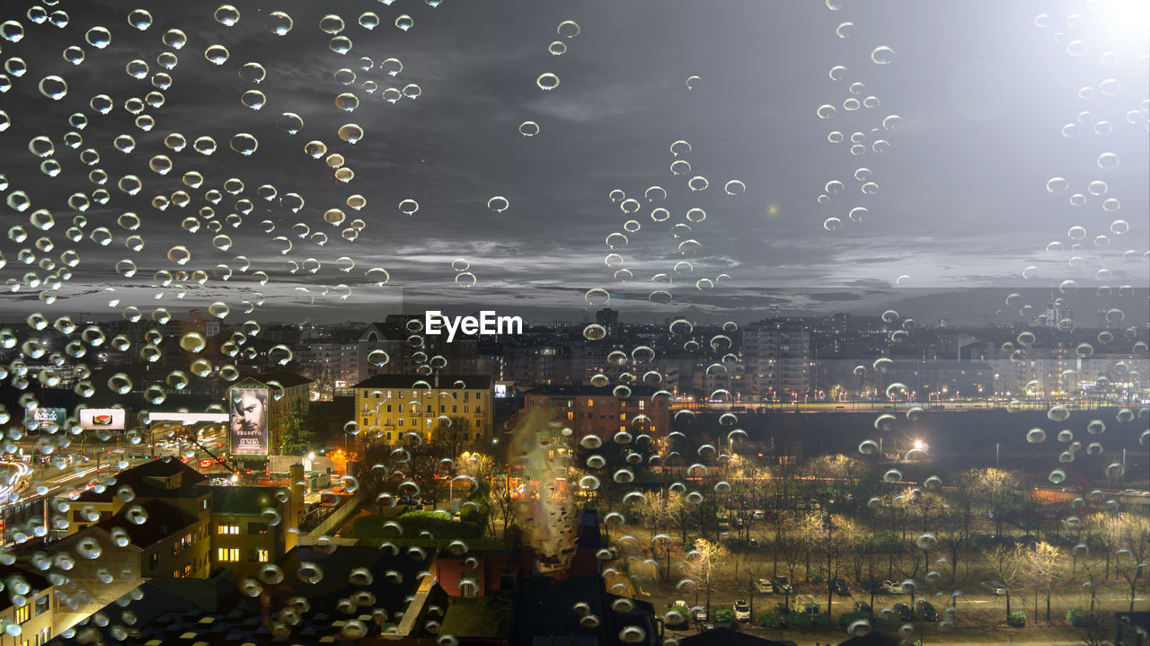 CLOSE-UP OF WET ILLUMINATED CITYSCAPE AGAINST SKY