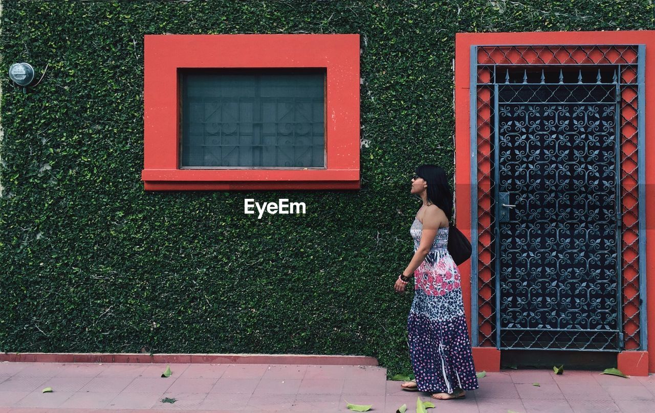 Side view of woman walking against green wall