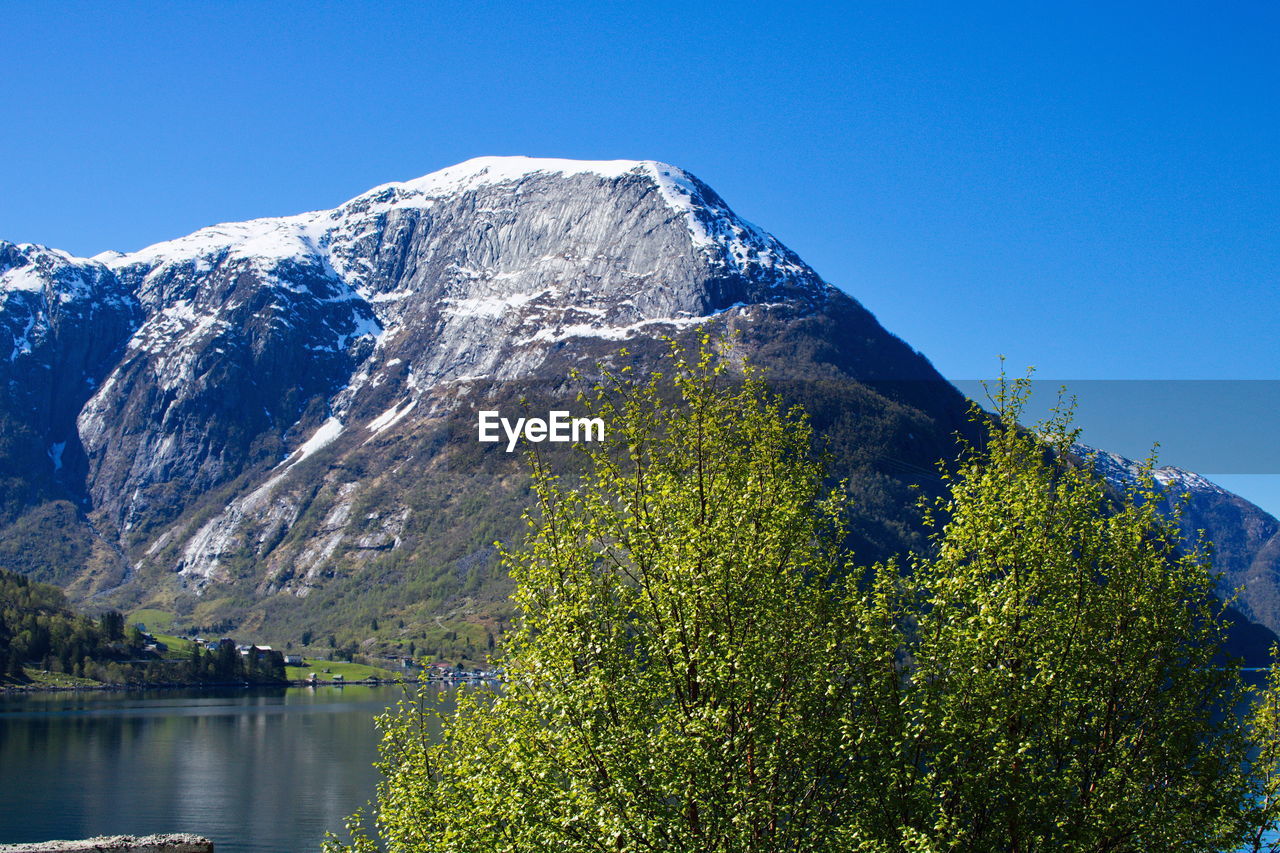 Scenic view of lake and mountains against clear blue sky