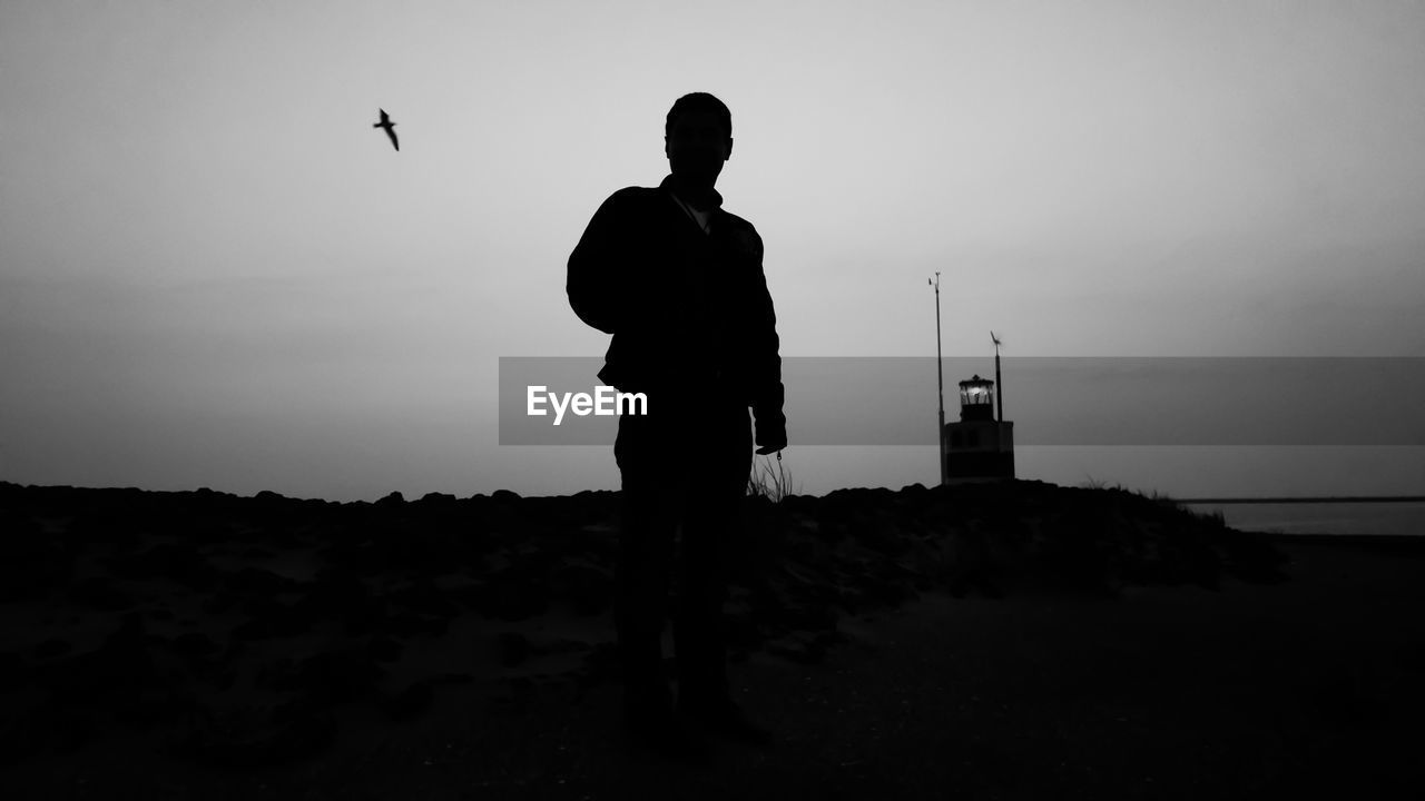 Silhouette man standing by sea against sky during sunset