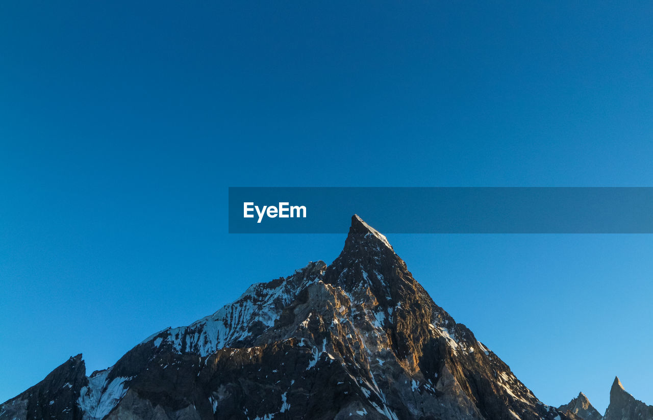 Low angle view of snowcapped mountains against clear blue sky