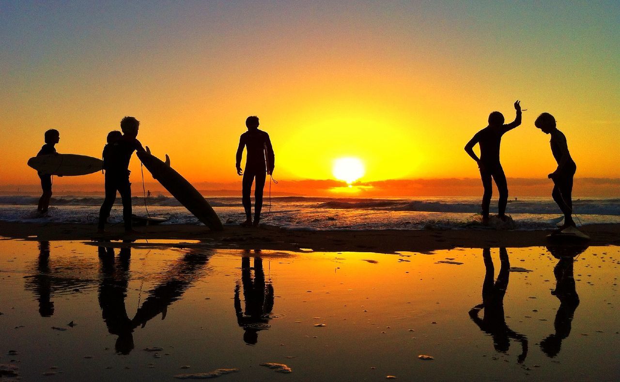 Silhouette people with surfboards walking on beach at sunset