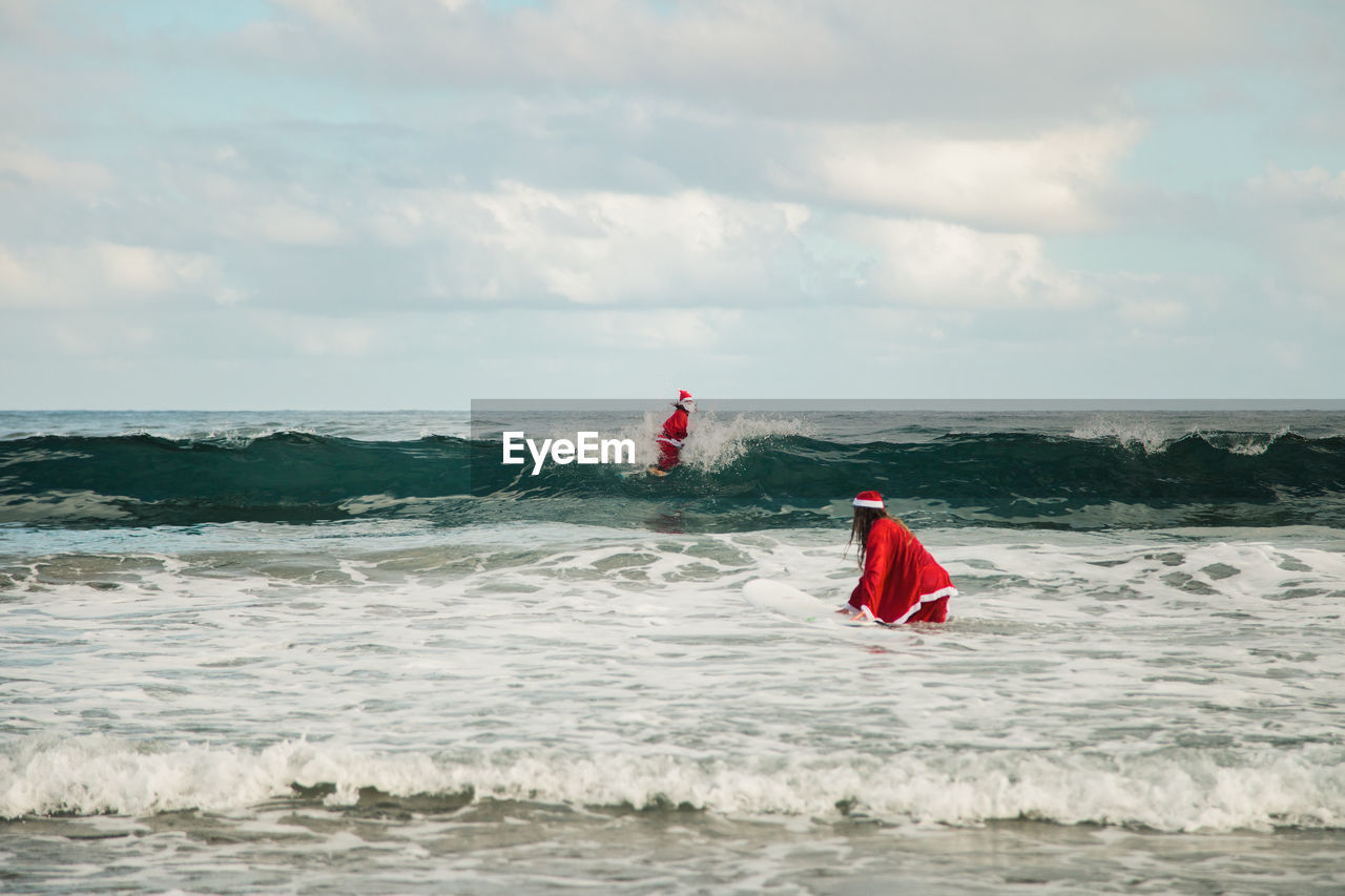 Couple wearing santa costumes surfing on sea