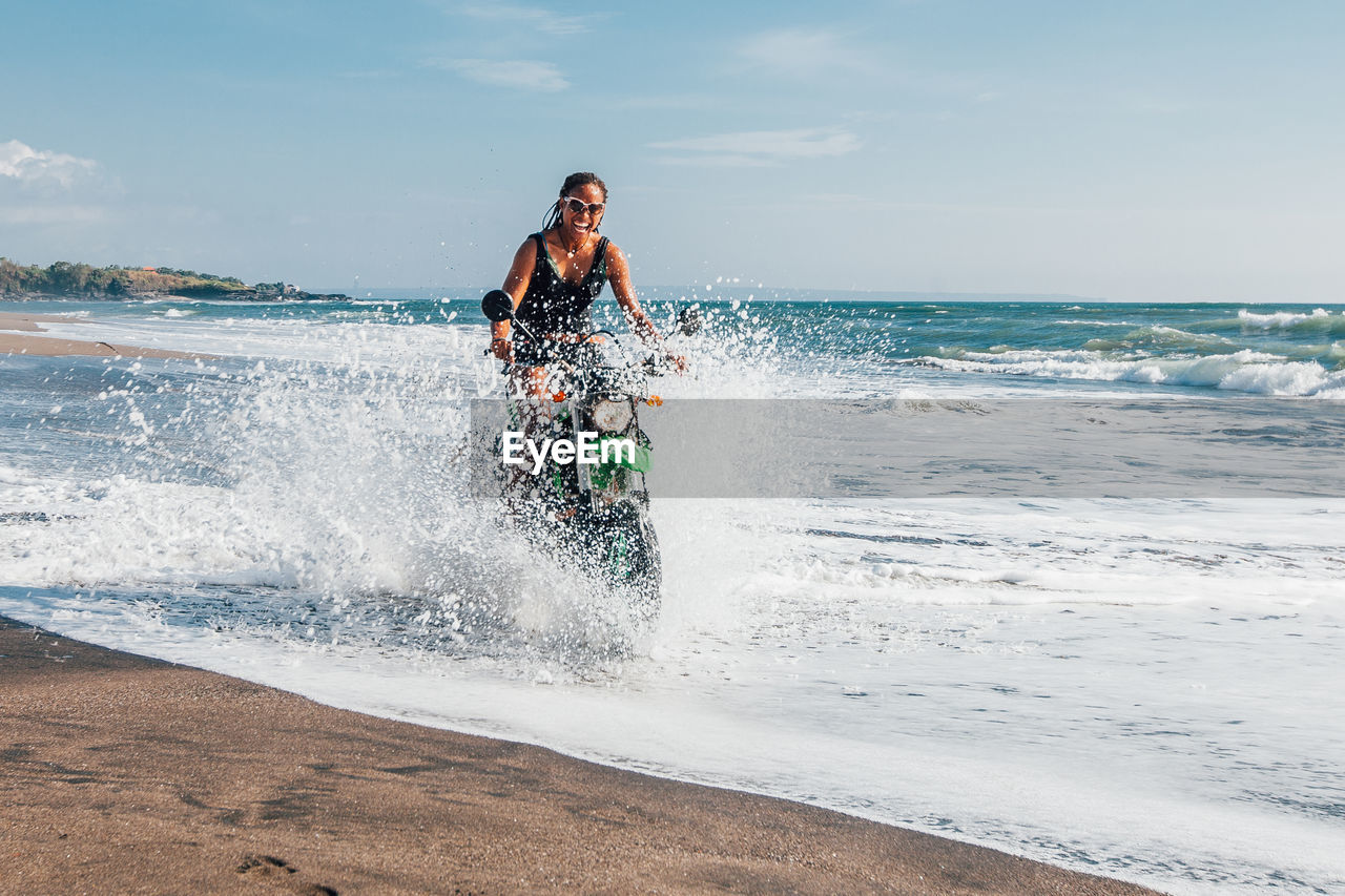 Young woman splashing water while riding motorcycle at beach