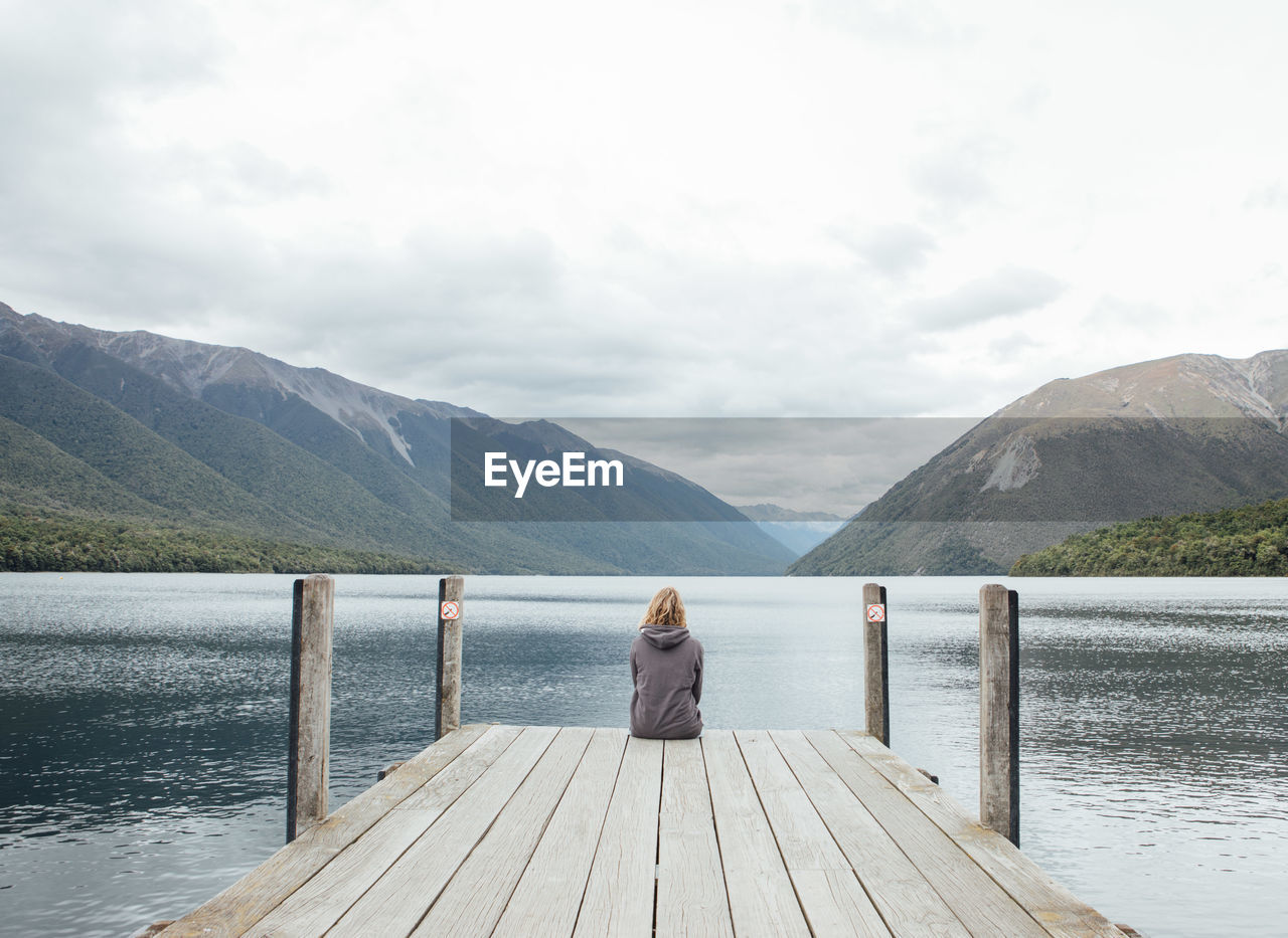 Rear view of woman sitting on pier over lake