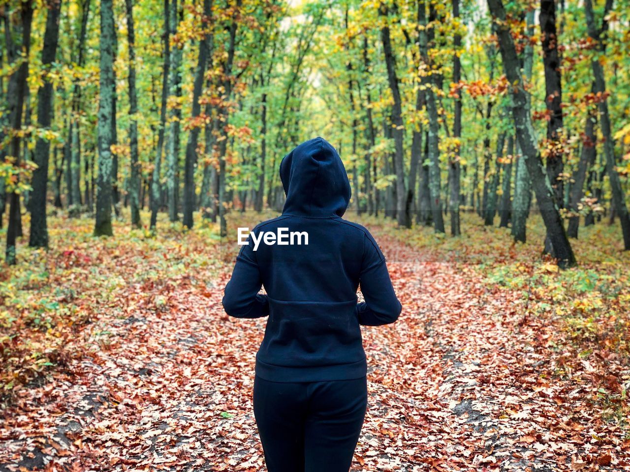 Back of woman wearing black tracksuit with hoodie standing alone in the middle of the forest