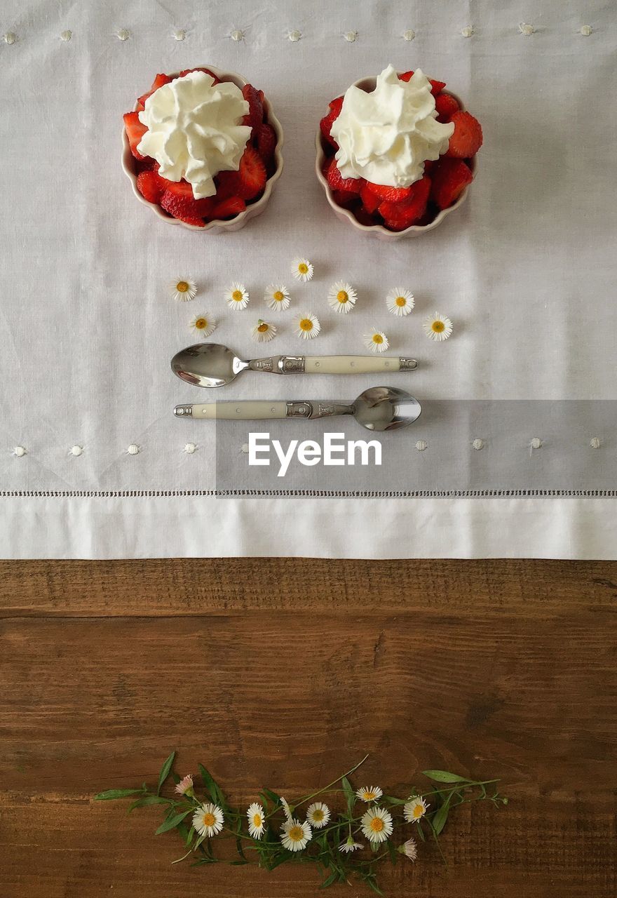 Directly above shot of strawberries with whipped creams in bowls on table