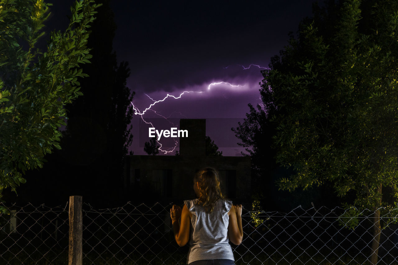 Rear view of woman looking at thunderstorm in night