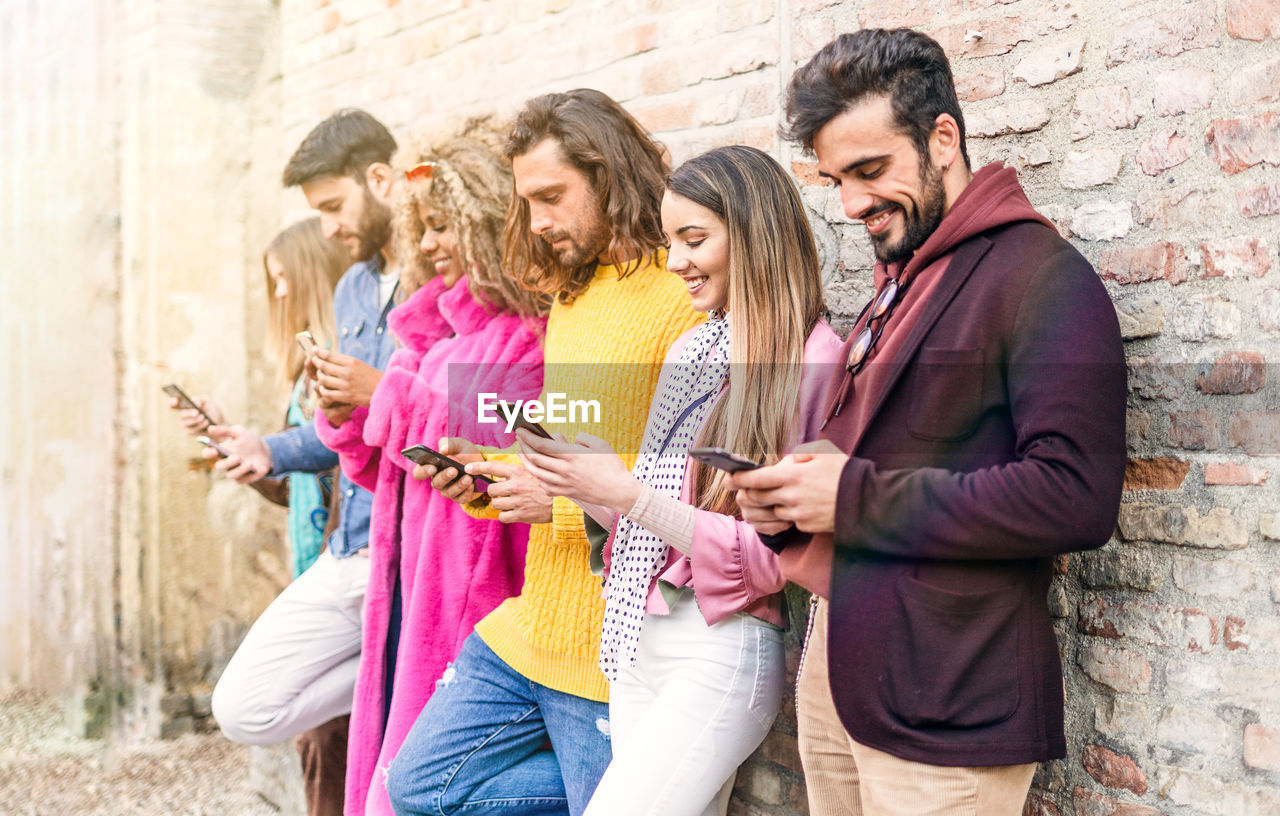 Friends using mobile phone while standing against wall