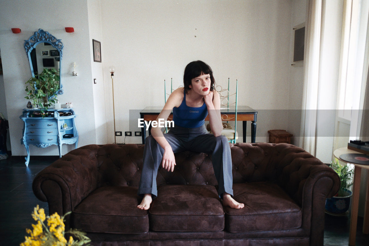 PORTRAIT OF YOUNG WOMAN SITTING ON SEAT AT HOME