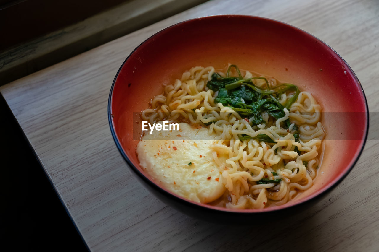 A bowl of instant noodles with eggs and vegetables by the window