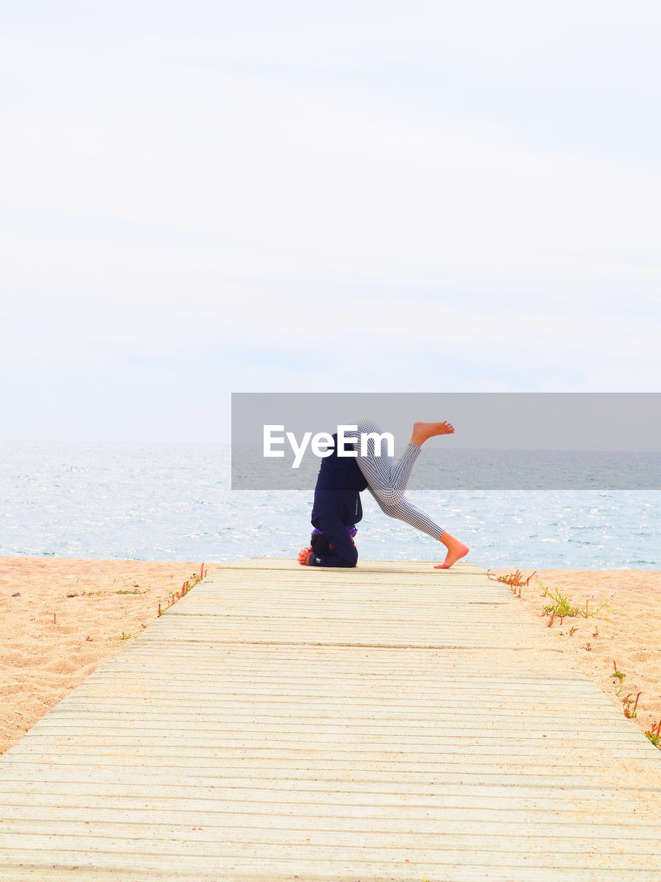 Full length of woman practicing headstand at beach against sky