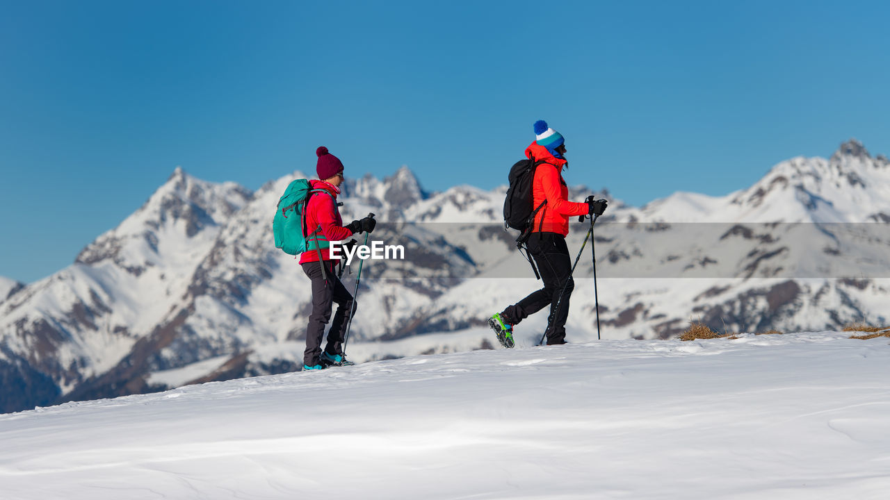 REAR VIEW OF PEOPLE ON SNOWCAPPED MOUNTAIN AGAINST SKY