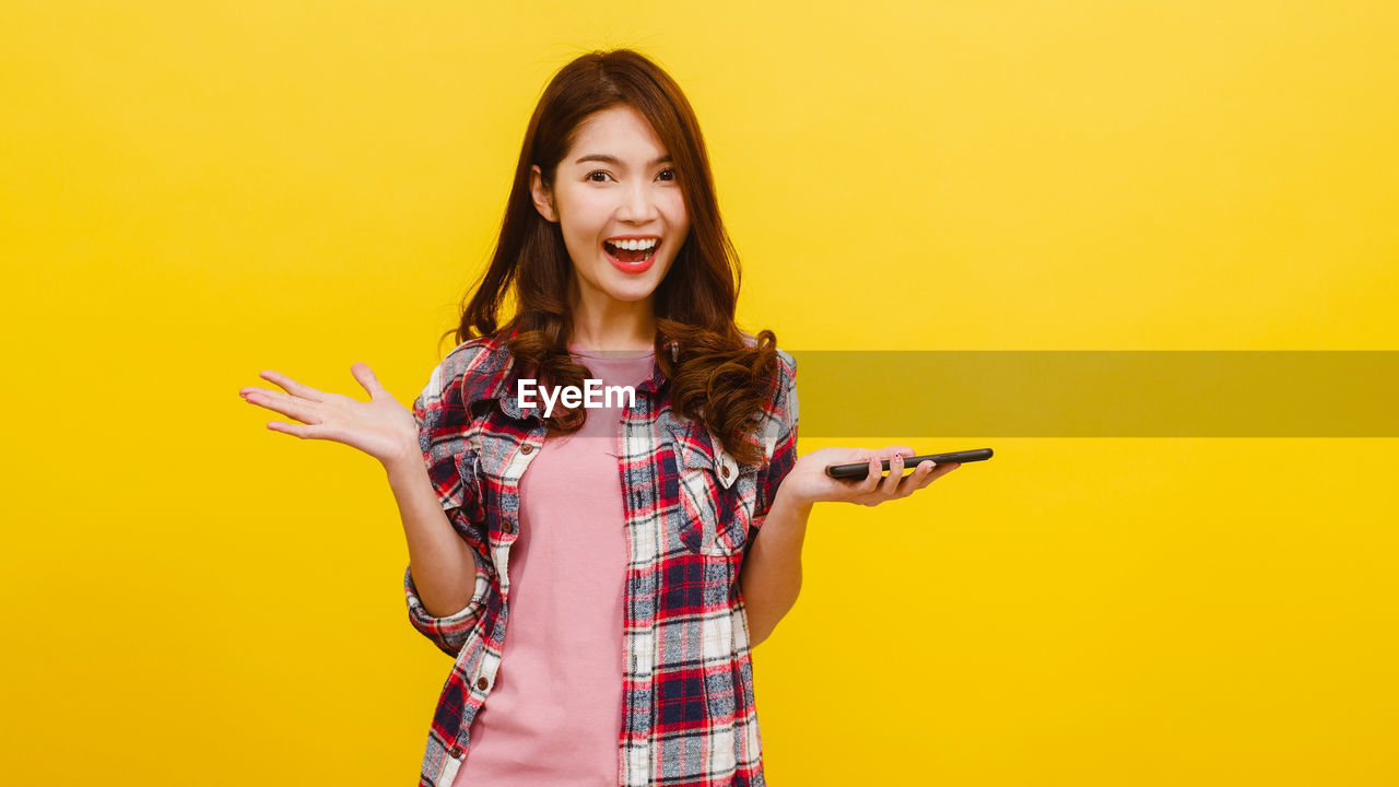 PORTRAIT OF SMILING YOUNG WOMAN AGAINST YELLOW GRAY BACKGROUND AGAINST ORANGE WALL