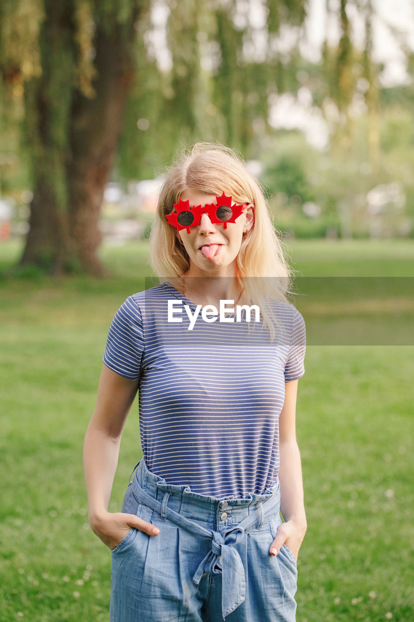 Portrait of woman sticking out tongue while standing at park