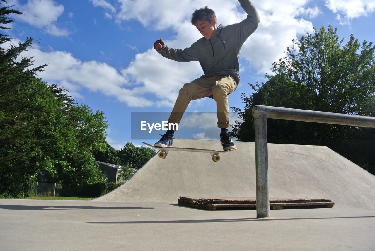 Boy skateboarding at skateboard park against sky