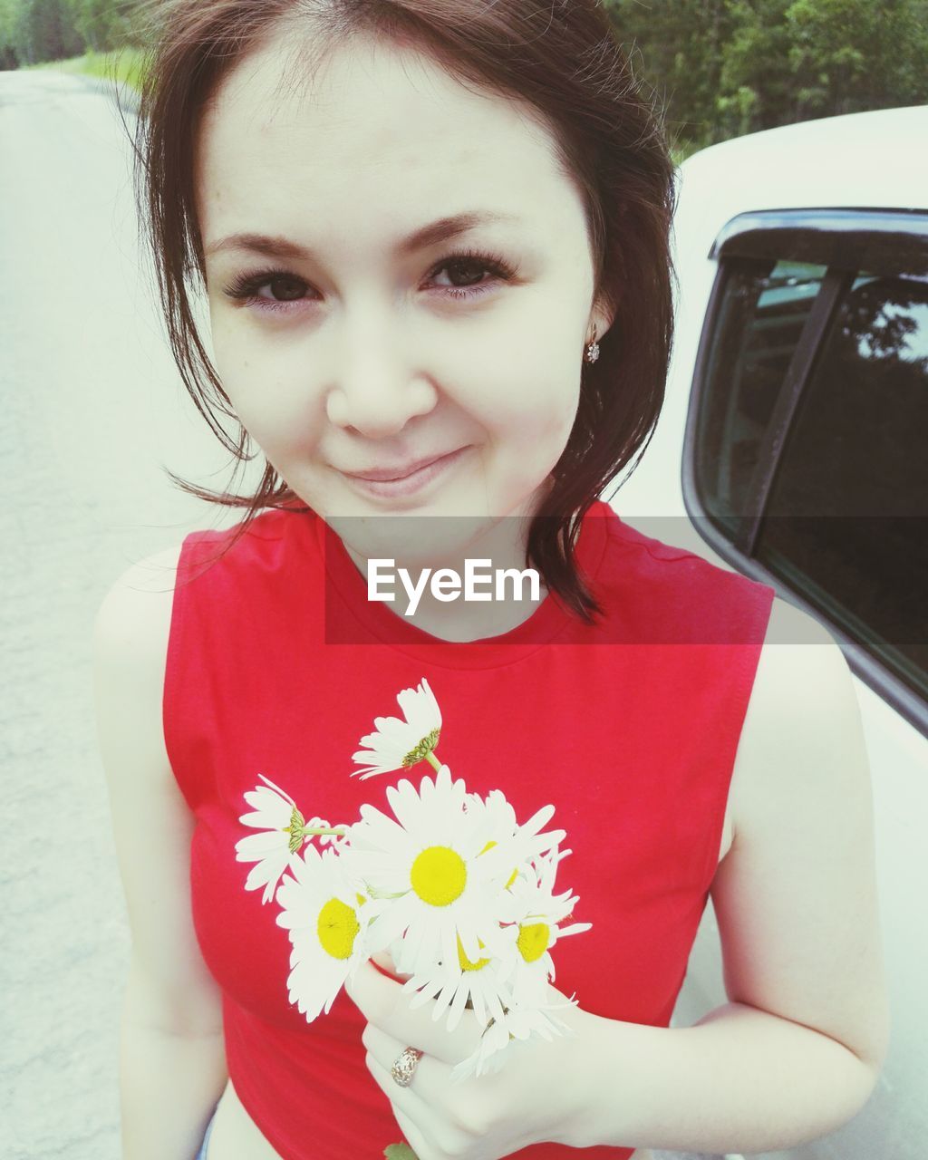 Portrait of young woman holding flowers by car on road