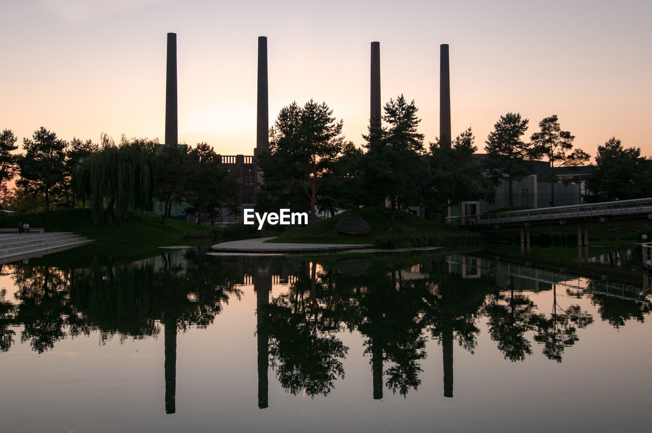 Reflection of chimneys on calm lake during sunset