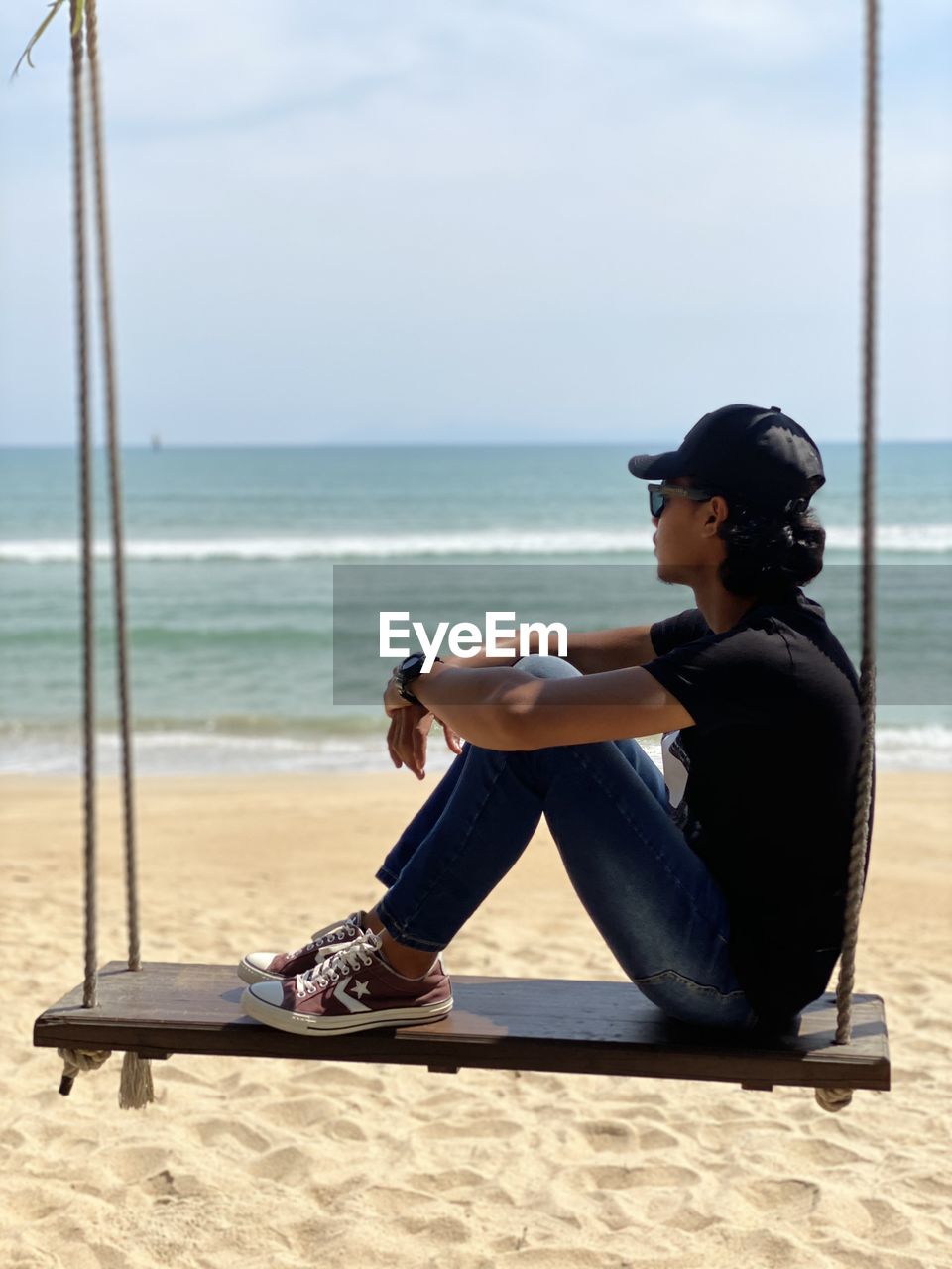 SIDE VIEW OF MAN SITTING ON SHORE AT BEACH