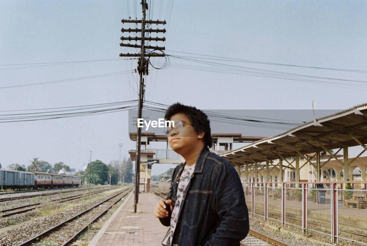 Side view of man standing at railroad station against sky