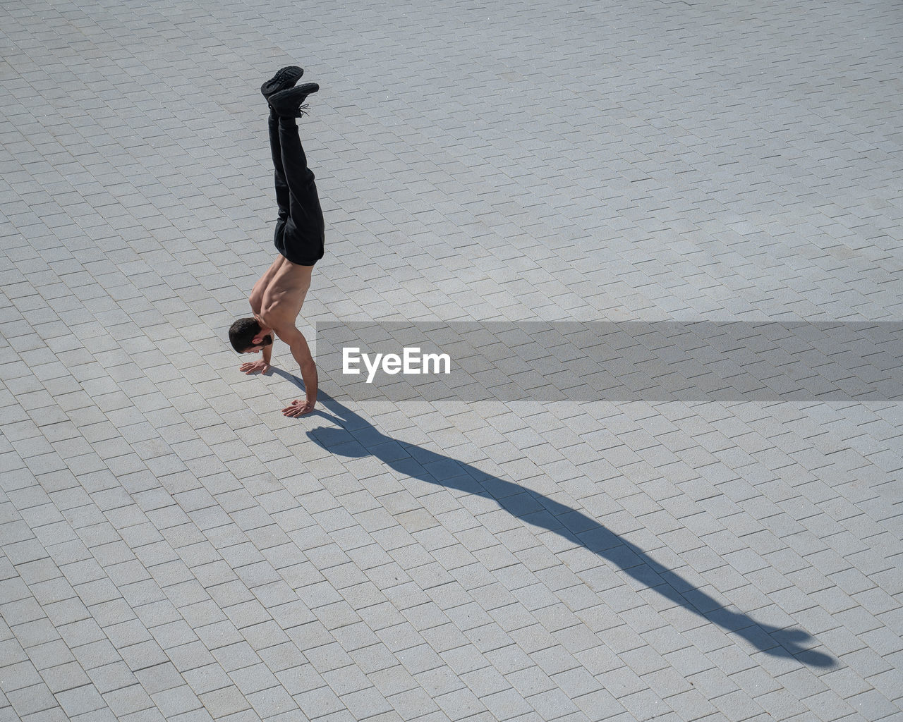 Shirtless man walks on his hands outdoors. view from above.